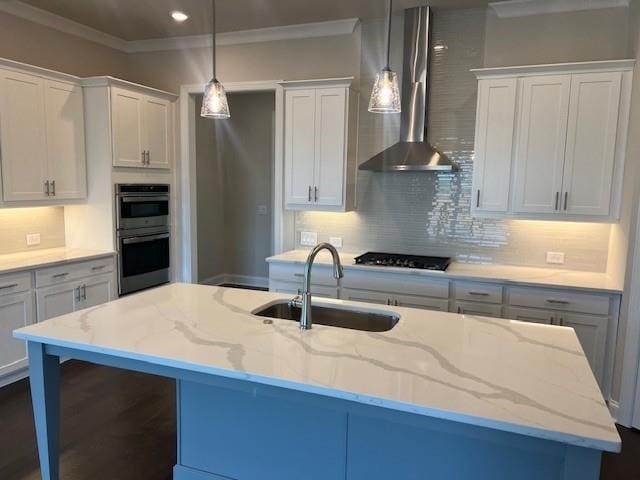 kitchen featuring light stone countertops, stainless steel double oven, a sink, an island with sink, and wall chimney exhaust hood