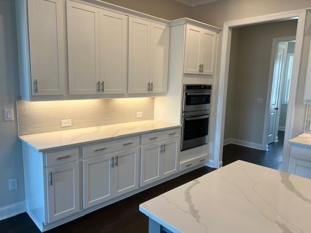 kitchen featuring decorative backsplash, light stone counters, baseboards, double oven, and white cabinetry