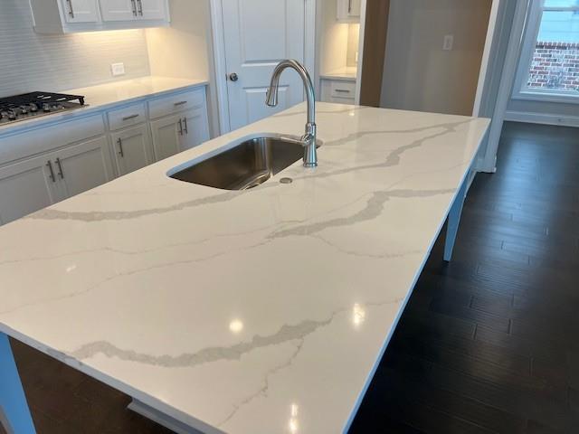 kitchen featuring a large island, stainless steel gas cooktop, dark wood finished floors, a sink, and white cabinetry