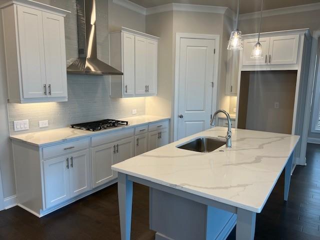 kitchen with white cabinets, a sink, wall chimney exhaust hood, stainless steel gas stovetop, and ornamental molding
