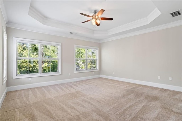 empty room featuring ceiling fan, ornamental molding, a raised ceiling, and light carpet