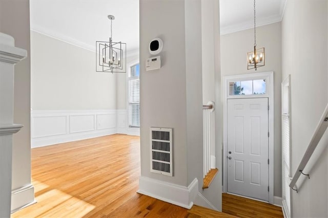 entryway with hardwood / wood-style floors, crown molding, and a chandelier