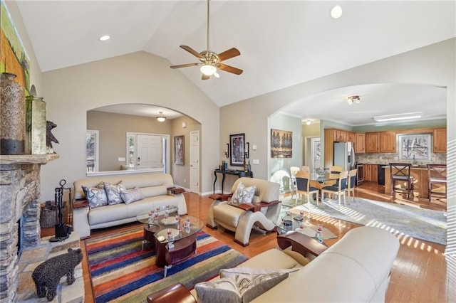 living room with ceiling fan, lofted ceiling, a stone fireplace, and light wood-type flooring