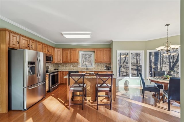 kitchen with a notable chandelier, a kitchen island, hanging light fixtures, appliances with stainless steel finishes, and a breakfast bar area