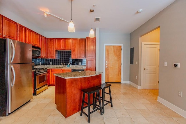 kitchen featuring a kitchen bar, appliances with stainless steel finishes, light stone countertops, a kitchen island, and hanging light fixtures