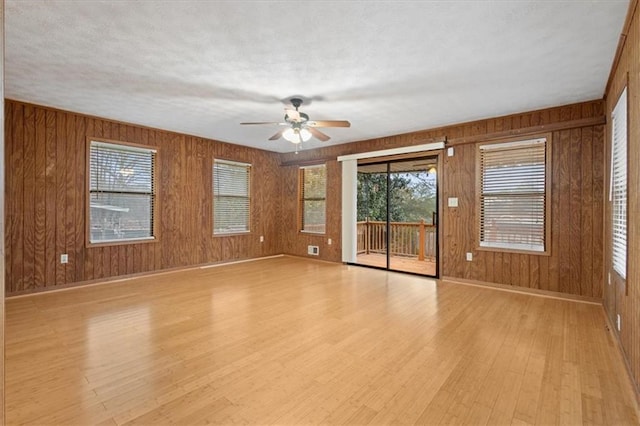 spare room with wooden walls, a ceiling fan, baseboards, and light wood-style flooring