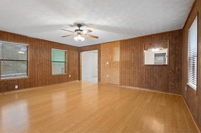empty room featuring wooden walls, ceiling fan, light wood-type flooring, and a healthy amount of sunlight
