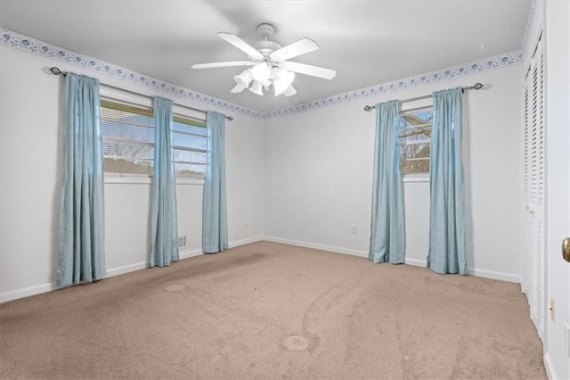 empty room with carpet floors, a ceiling fan, and baseboards