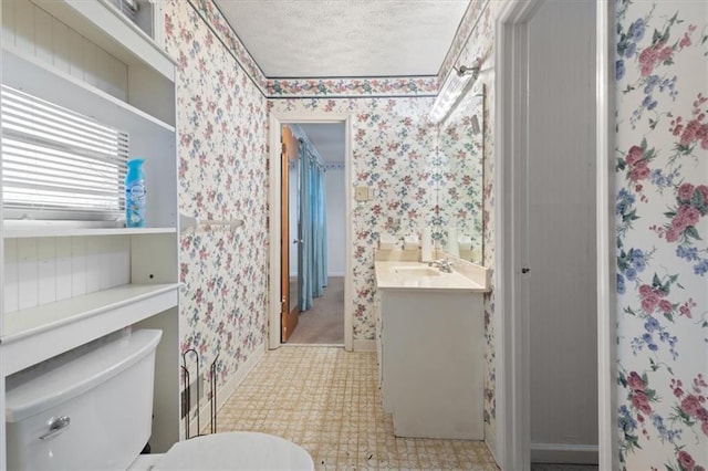 bathroom with vanity, toilet, baseboards, wallpapered walls, and a textured ceiling