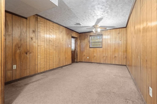 empty room with wood walls, baseboards, ceiling fan, a textured ceiling, and carpet flooring