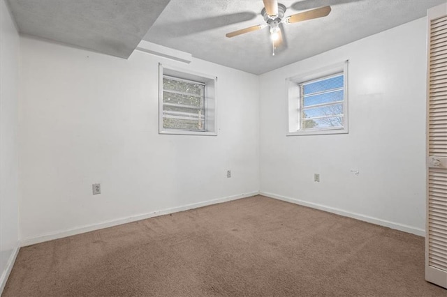 carpeted spare room featuring a ceiling fan, baseboards, and a wealth of natural light