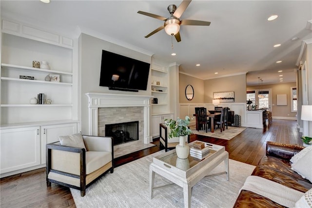 living room with dark wood-type flooring, crown molding, ceiling fan, built in features, and a fireplace