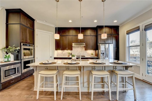 kitchen featuring light stone countertops, decorative light fixtures, stainless steel appliances, and a kitchen island with sink