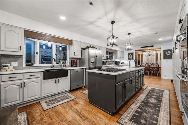 kitchen featuring light countertops, light wood-style flooring, appliances with stainless steel finishes, a sink, and an island with sink