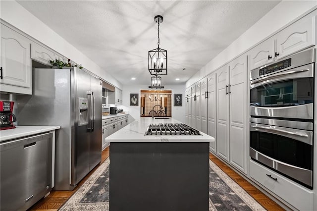 kitchen featuring white cabinets, a kitchen island, decorative light fixtures, light stone countertops, and stainless steel appliances