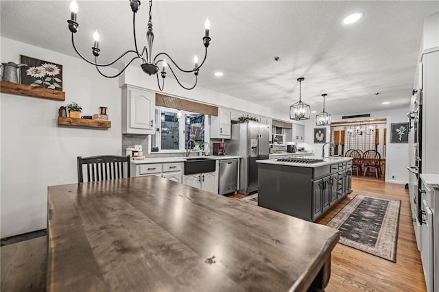 kitchen featuring gray cabinetry, a kitchen island, hanging light fixtures, appliances with stainless steel finishes, and open shelves