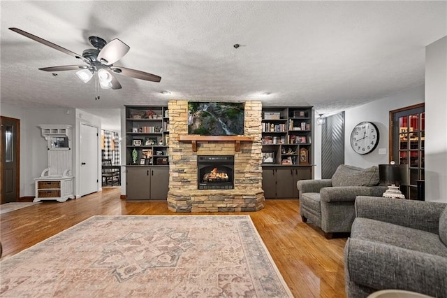 living area featuring built in shelves, a fireplace, ceiling fan, a textured ceiling, and light wood-type flooring