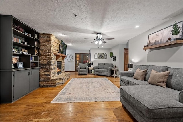 living room featuring light wood-type flooring, ceiling fan, a textured ceiling, and a stone fireplace