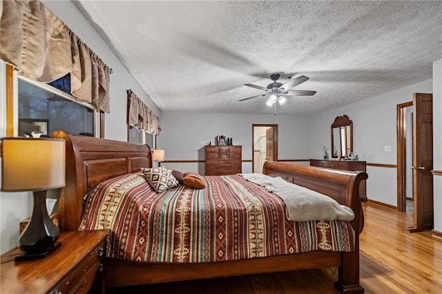 bedroom with a textured ceiling, ceiling fan, light wood-type flooring, and baseboards