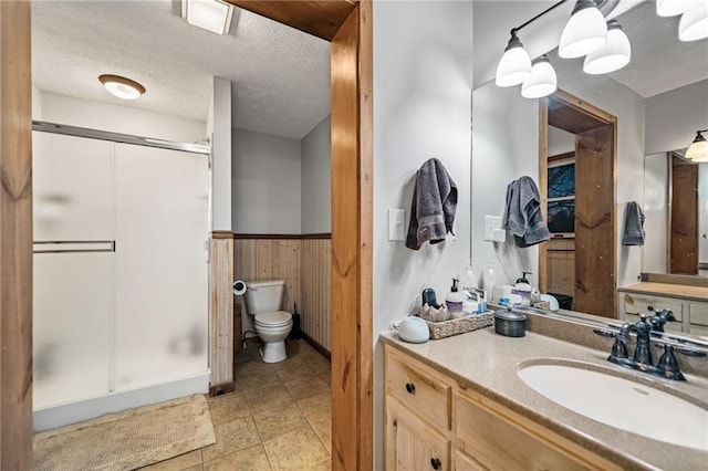 bathroom with wainscoting, a textured ceiling, vanity, wood walls, and a shower stall