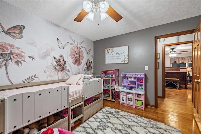 bedroom featuring ceiling fan, a textured ceiling, baseboards, and wood finished floors