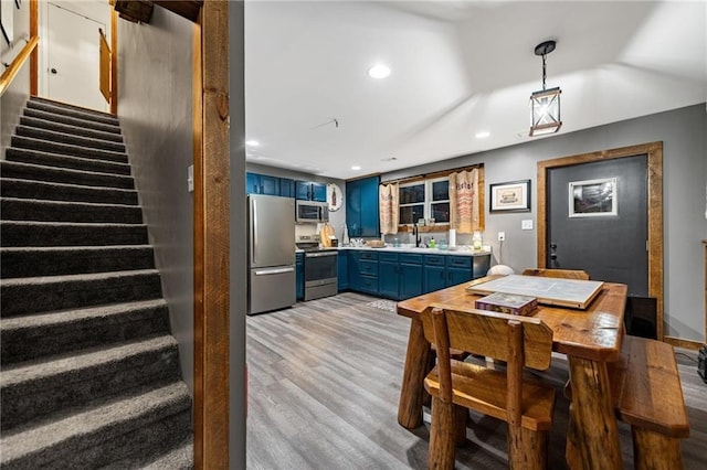 kitchen featuring blue cabinets, stainless steel appliances, light countertops, light wood-style floors, and pendant lighting