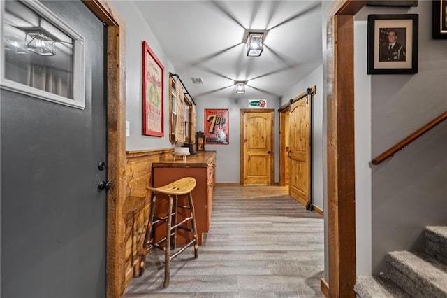 corridor featuring light wood finished floors, a barn door, stairs, and visible vents