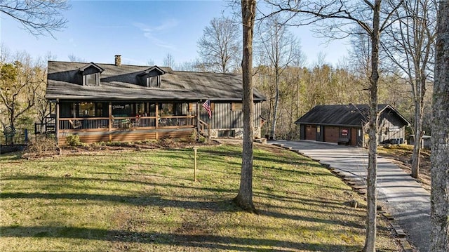 view of front of property featuring an outbuilding, a chimney, covered porch, a garage, and a front lawn