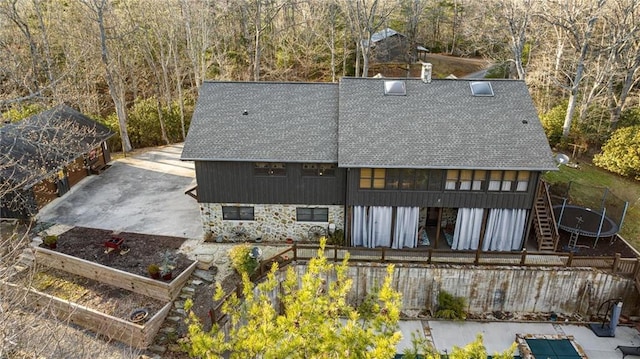 rear view of property featuring stairs, stone siding, a garden, and roof with shingles