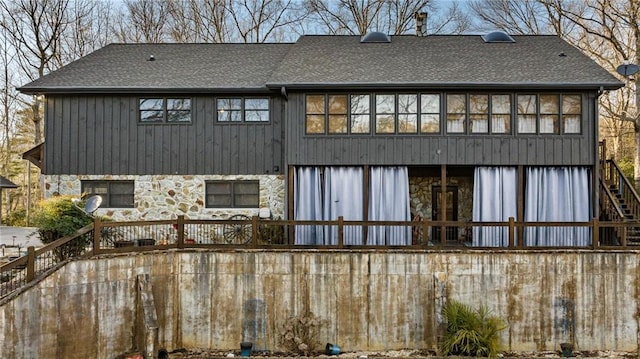 rear view of property featuring stairs, stone siding, and roof with shingles