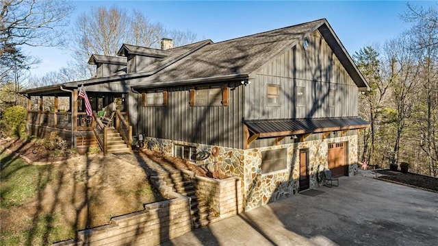 view of side of property featuring a garage, driveway, stone siding, stairway, and a chimney