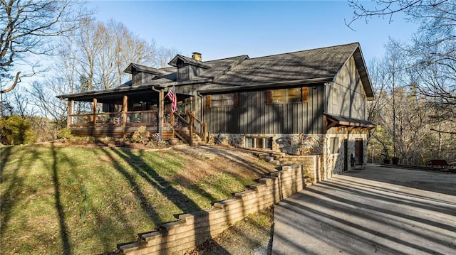 view of front of house featuring driveway, covered porch, a chimney, and a front yard