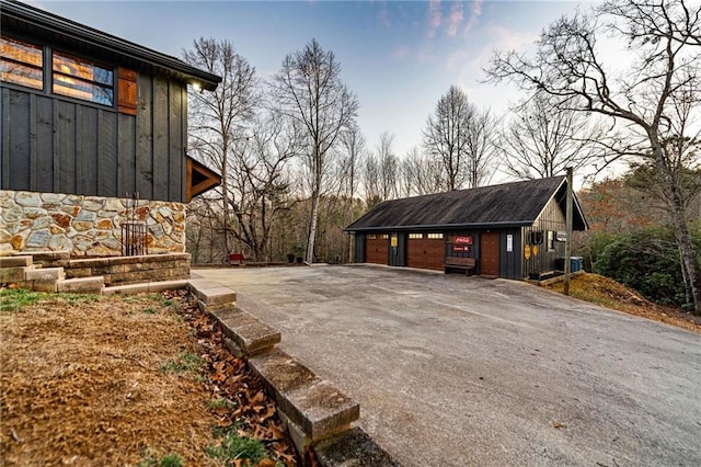 view of side of home featuring a garage, stone siding, board and batten siding, and an outbuilding