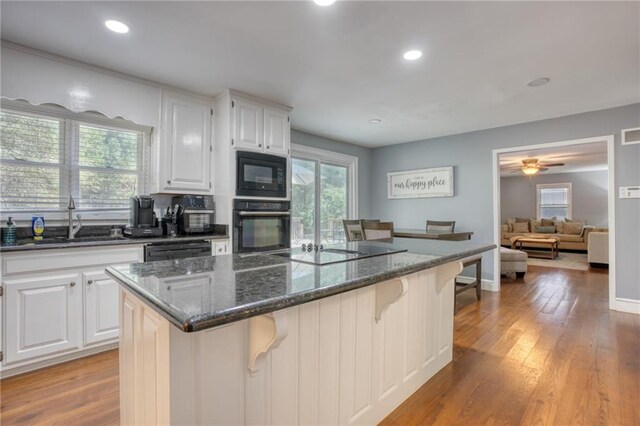 kitchen featuring a breakfast bar, a center island, black appliances, white cabinets, and dark stone countertops