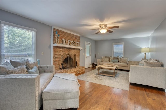 living room featuring wood-type flooring, a brick fireplace, and ceiling fan