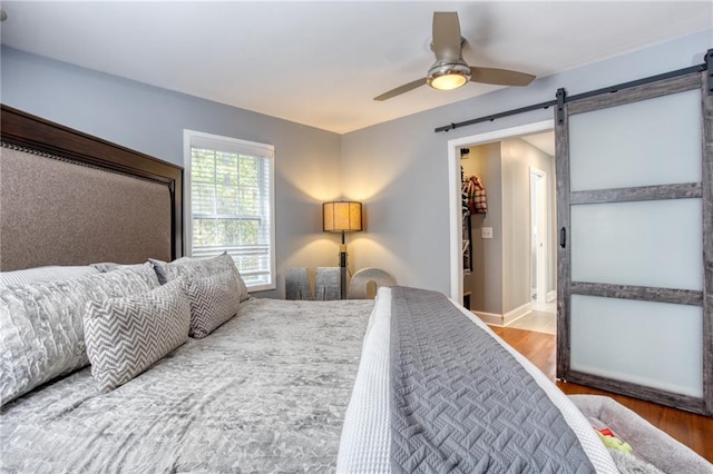 bedroom featuring hardwood / wood-style floors, ceiling fan, a barn door, and a spacious closet