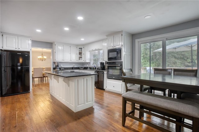 kitchen featuring a kitchen bar, black appliances, an inviting chandelier, white cabinets, and hardwood / wood-style floors