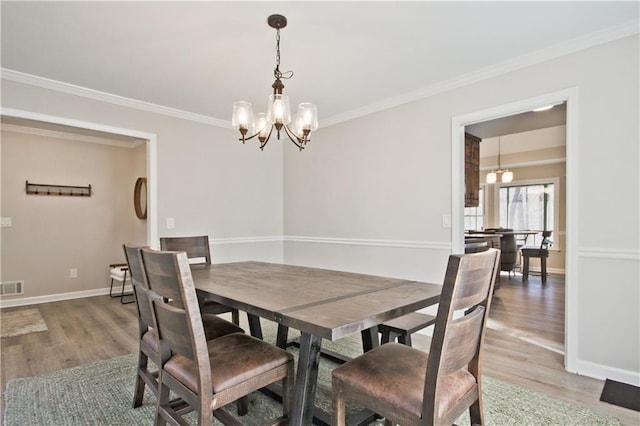 dining area with baseboards, visible vents, an inviting chandelier, ornamental molding, and light wood-type flooring