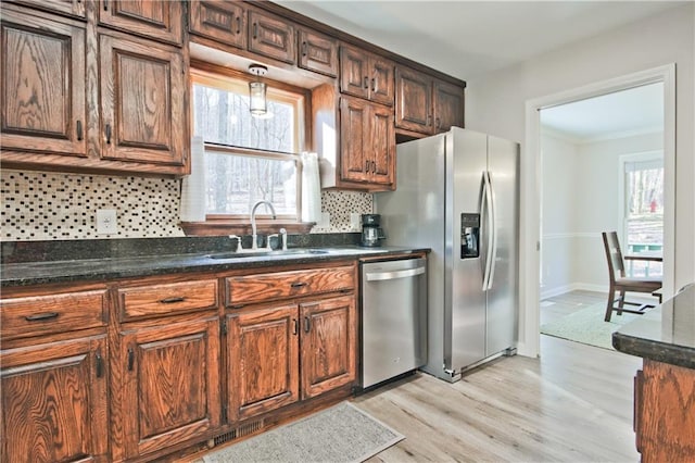 kitchen featuring light wood-type flooring, a sink, stainless steel appliances, decorative backsplash, and a healthy amount of sunlight