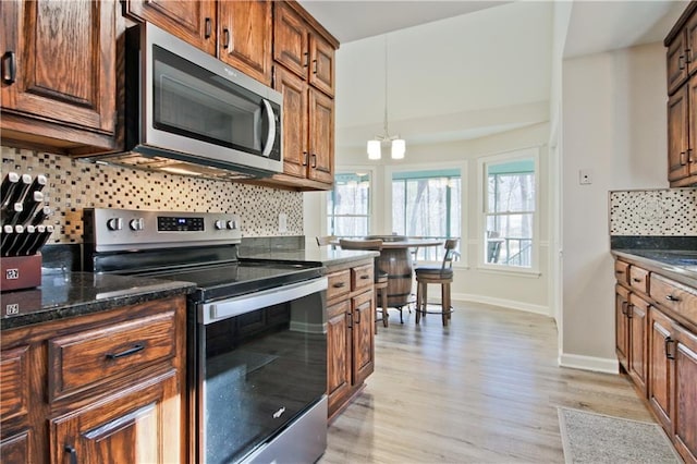 kitchen featuring baseboards, dark stone counters, light wood-style flooring, appliances with stainless steel finishes, and backsplash