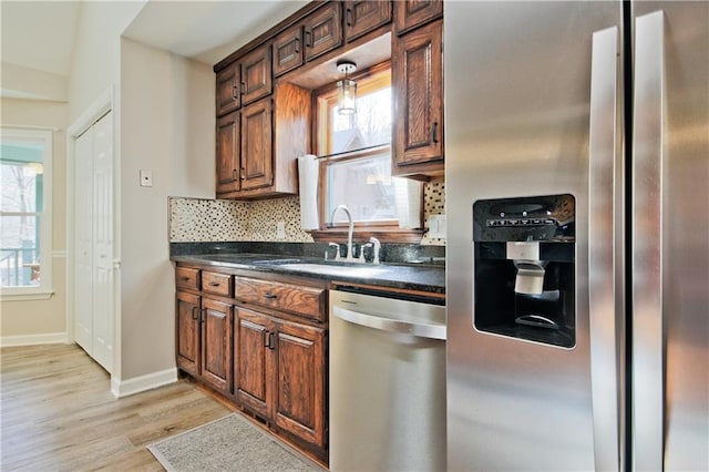 kitchen with a sink, light wood-style floors, appliances with stainless steel finishes, dark countertops, and tasteful backsplash