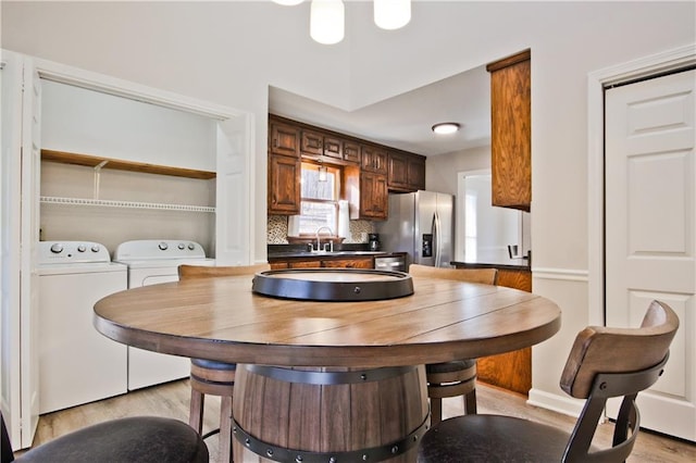 kitchen featuring independent washer and dryer, stainless steel refrigerator with ice dispenser, a sink, tasteful backsplash, and light wood-style floors