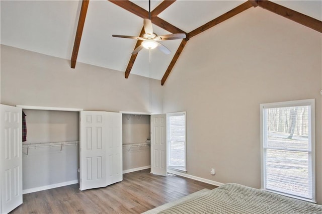 unfurnished bedroom featuring beam ceiling, wood finished floors, two closets, and high vaulted ceiling