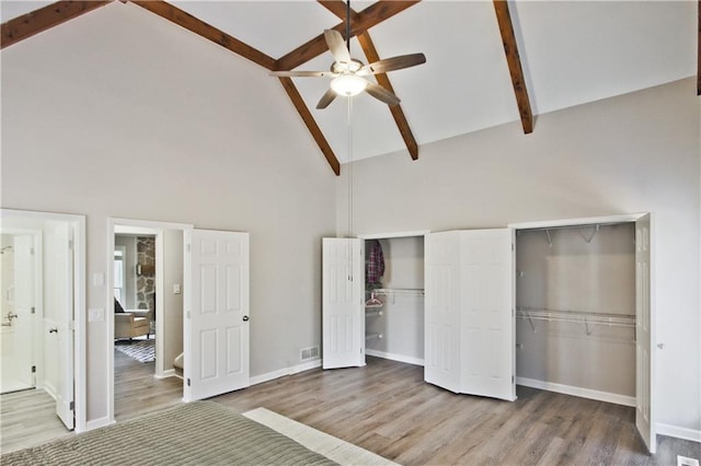 unfurnished bedroom with wood finished floors, baseboards, high vaulted ceiling, beamed ceiling, and two closets