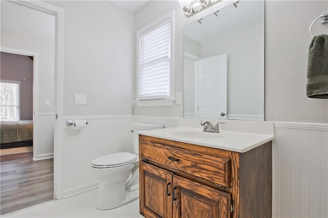 ensuite bathroom featuring a wainscoted wall, toilet, vanity, wood finished floors, and ensuite bath