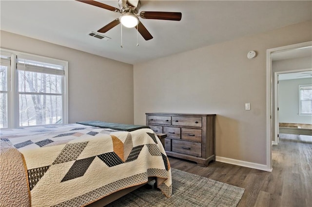 bedroom featuring dark wood-style floors, visible vents, a ceiling fan, and baseboards