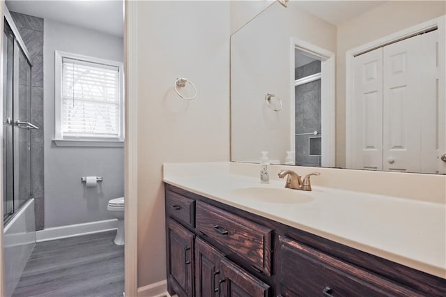 full bathroom featuring toilet, wood finished floors, baseboards, bath / shower combo with glass door, and vanity