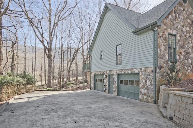 view of side of property with concrete driveway, an attached garage, stone siding, and roof with shingles