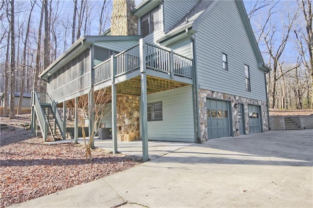 view of property exterior featuring stone siding, stairway, concrete driveway, a garage, and a chimney