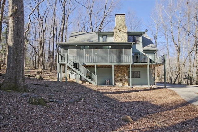 rear view of property featuring stairway, driveway, a sunroom, and a chimney